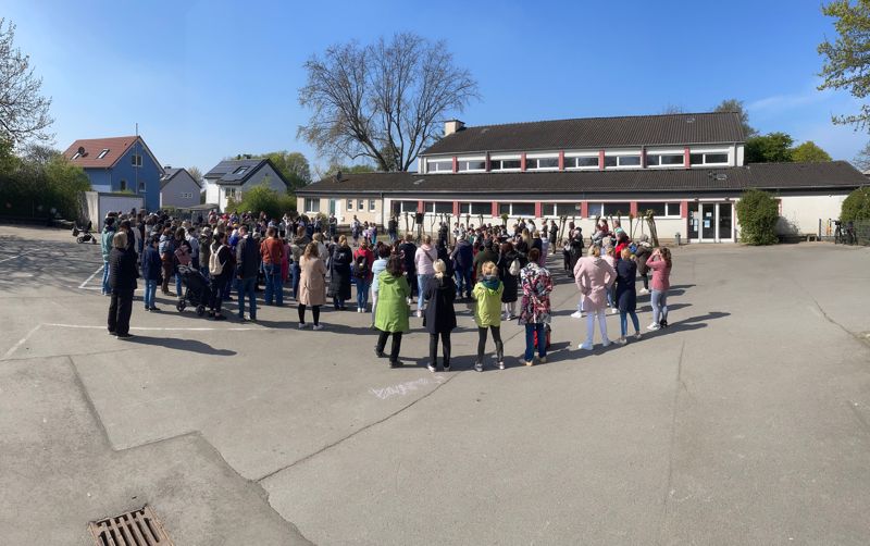 Kinder, Eltern und Lehrkräfte versammelt auf dem Schulhof der GGS Millrath
